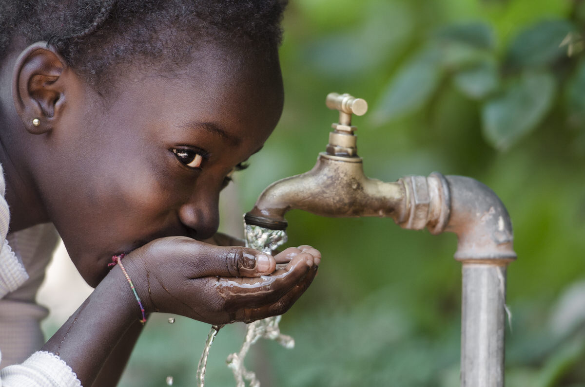 Imagem de uma criança contente bebendo água em torneira.